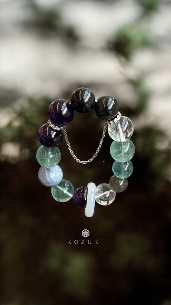 Green jade crystal bracelet with white jade ring centerpiece resting against dark moss background