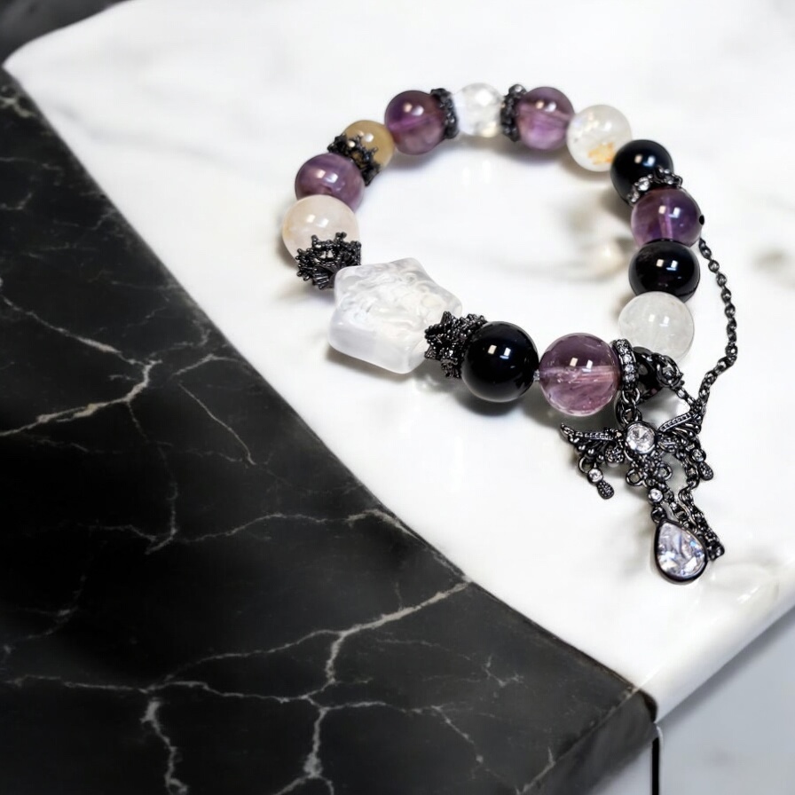 Purple crystal wing bracelet made with phantom amethyst and obsidian, photographed on black and white marble