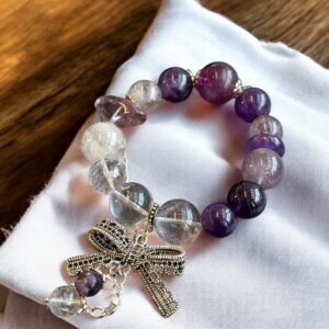 Amethyst and clear quartz gemstone bracelet featuring a silver bow charm and dangle chain on white fabric