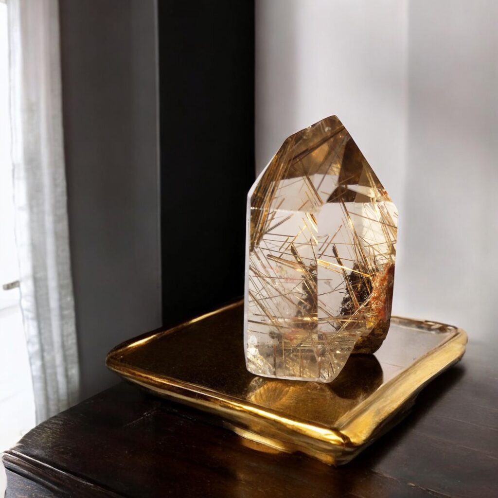 Golden rutilated quartz crystal with angular cuts resting on a golden ceramic tray, glowing under soft daylight — a grounding yet radiant energy piece.