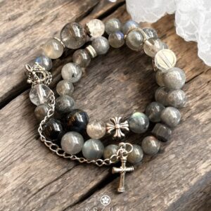 Labradorite and rutilated quartz crystal bracelet with sterling silver cross charm and crown detail on wooden surface with lace background
