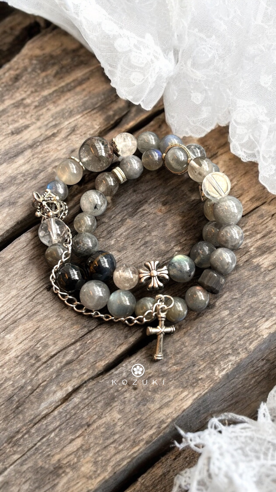 Labradorite and rutilated quartz crystal bracelet with sterling silver cross charm and crown detail on wooden surface with lace background